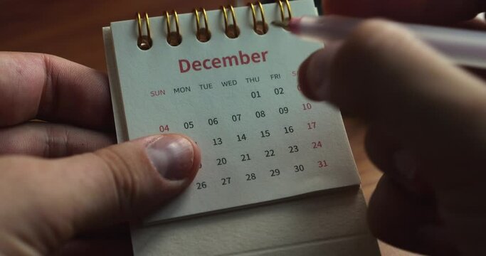Close-up of male hands flipping a rollover calenda, brightly highlighting the important date in December 15 with a red pen. Deadline concept, meeting. Event reminder. Organization and time management