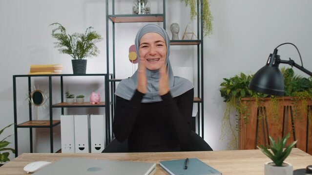 Happy young muslim business woman wearing hijab headscarf shouting, celebrating success victory, winning, goal achievement, good news, lottery jackpot luck, surprise. Girl at home office workspace