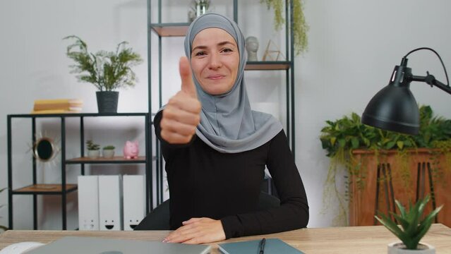 Like. Happy young muslim business woman wearing hijab headscarf looking approvingly at camera showing thumbs up, like sign positive something good, positive feedback. Girl at home office workspace