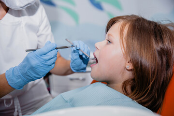 A woman dentist in a white coat and and blue gloves treats the teeth of European appearance girl in...