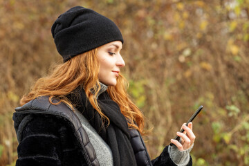 young woman with mobile phone in autumn park. Black hat and scarf.