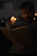 selective focus of book near man holding lit candle while reading during electricity shutdown.