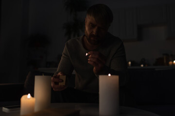 man holding lit match near burning candles while sitting in kitchen during power outage.