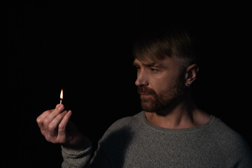 man looking at flame of burning match during energy blackout isolated on black.