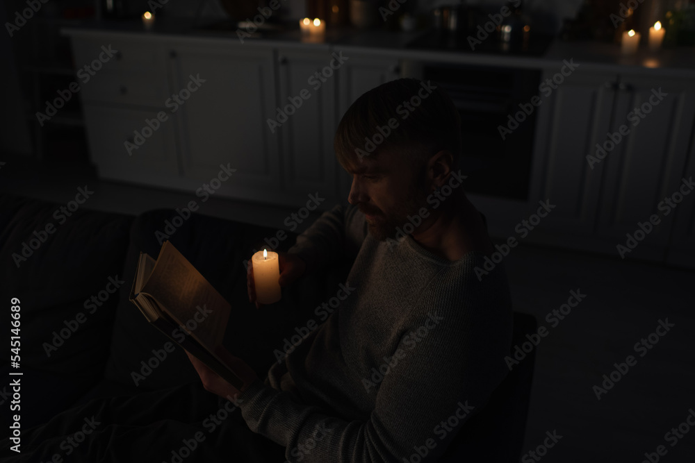 Wall mural high angle view of man reading book during electricity shutdown in kitchen with burning candles.