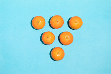Juicy, natural and irregular tangerines on a blue background, with copy space, forming a triangle shape in a pop art style