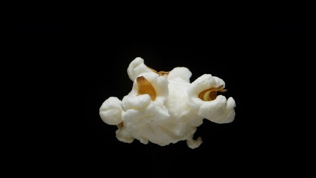 A single grain of popcorn rotates on a black background, close-up.