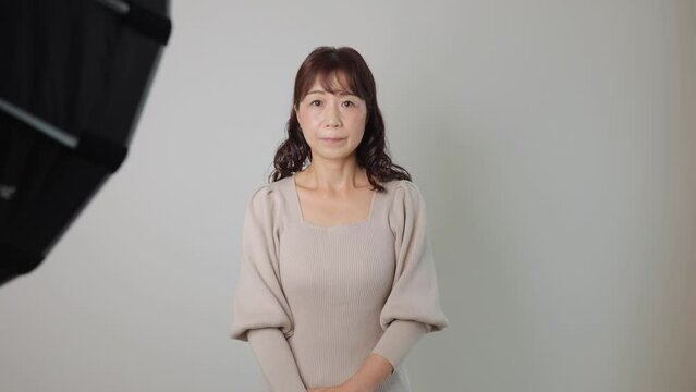 Middle aged asian woman stand still and stars the camera at photo studio. White wall. 25P