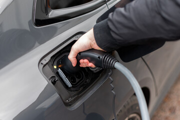 Close up of electric vehicle plug in charge stop - Modern EV charging cable with man putting cable...