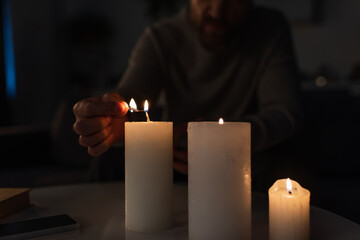 partial view of man lighting candles near mobile phone on table during electricity outage.