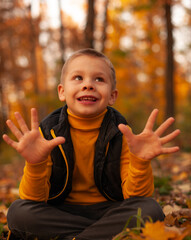 The boy in the autumn park sitting on the yellow foliage