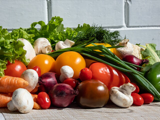 A pile of fresh, healthy and colorful vegetables in bright sunlight with white brick wall in background. Tomatoes, onions, carrots, peppers, cauliflower, salad, dill and champignons