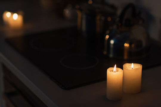 burning candles on kitchen worktop near stove in darkness caused by power outage.