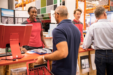 Male and female cashier talking with customers at checkout counter in hardware store
