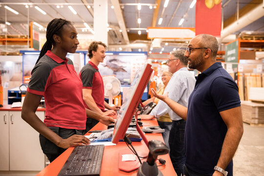 Male customer gesturing and talking with female cashier while standing at checkout counter in hardware store