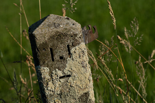 Grenzstein mit Gesicht, die aus L&ouml;chern bestehen, am Rand einer Wiese, in der Sonne