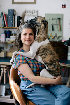 Portrait of smiling woman embracing dog while sitting on chair at home