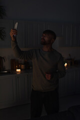 man standing with smartphone in raised hand while searching for mobile signal during electricity...