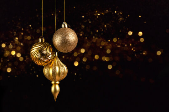 Christmas card with three golden balls decorations on black background with bokeh lights