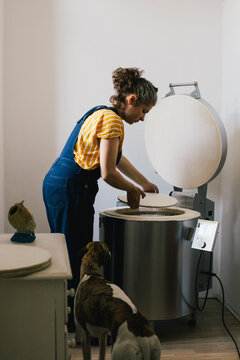 Side view of female craftsperson putting ceramic plate in electric kiln while working at home