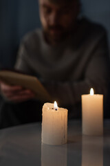 blurred man reading book in darkness near burning candles during energy blackout.
