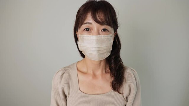 Asian middle aged woman reluctantly put her mask on. Unhappy, Tired, Disappointed. Dolly in. 25P