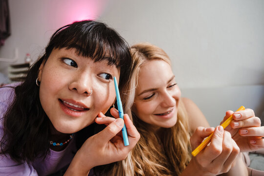 Two multiracial girls smiling and doing makeup at home