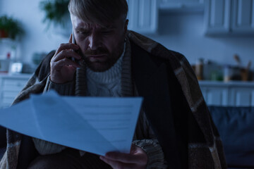 tense man talking on mobile phone while looking at payment bills during electricity shutdown.