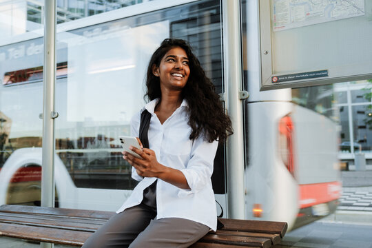 Young woman with backpack using cellphone while sitting at station