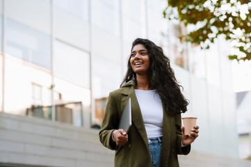 Brunette indian woman drinking coffee while walking on city street