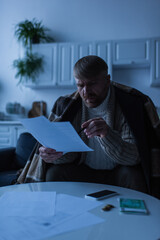 tense man pointing at payment bills near money and smartphone in kitchen.