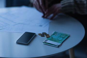 euro banknotes and coins near smartphone with blank screen and cropped man with payment bills on...