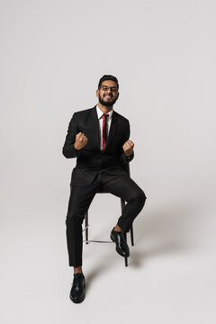 Excited indian man making winner gesture while sitting on chair