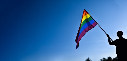 Rainbow flag, LGBT simbol, holding in hands of boy against clear bluesky background, soft and  selective focus, concept for LGBT celebration in pride month, June, around the world, copy space.