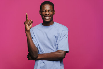 Black young man wearing t-shirt smiling and pointing finger upward