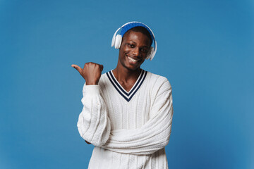 Black man pointing finger aside and listening music with headphones