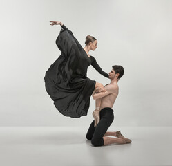 Young man and woman, ballet dancers performing isolated over grey studio background. Support. Beautiful wave