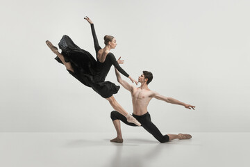 Young man and woman, ballet dancers performing isolated over grey studio background. Twine jump