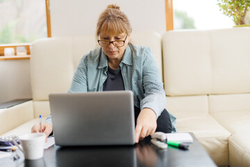 Active mature woman using a laptop for remote work from the home office. Video conference, video meeting. Senior teacher leads webinar