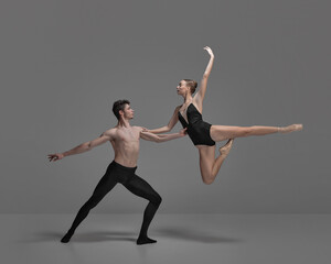 Young man and woman, ballet dancers performing isolated over dark grey studio background. Jumping high