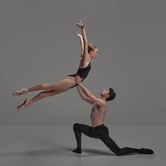 Young man and woman, ballet dancers performing isolated over dark grey studio background. Beautiful tender couple
