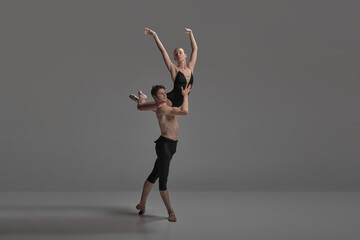 Young man and woman, ballet dancers performing isolated over dark grey studio background. Keeping balance on shoulder