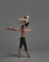 Young man and woman, ballet dancers performing isolated over dark grey studio background. Flying on...