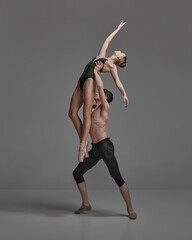 Young man and woman, ballet dancers performing isolated over dark grey studio background. Growing high