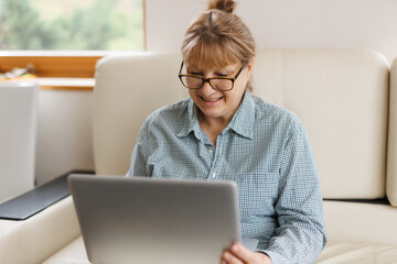 Active mature woman using a laptop for remote work from the home office. Video conference, video meeting. Senior teacher leads webinar