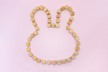 ピンクの背景で正面から見たウサギの形に並べたウッドキューブのフレーム