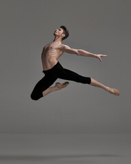 Portrait of young muscular man, ballet dancer performing isolated over dark grey studio background. Flying high