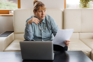 Active mature woman using a laptop for remote work from the home office. Video conference, video meeting. Senior teacher leads webinar