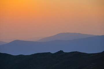 Obraz premium mountain chain silhouette in blue mist at the sunset, early morning mountain travel scene