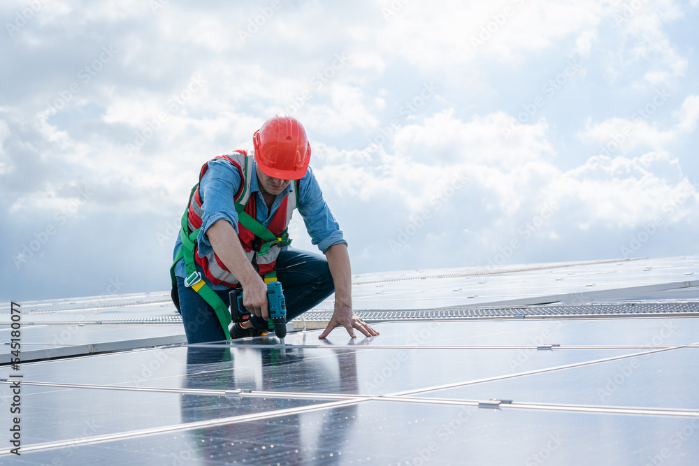 Poster technician wearing safety harness belt using drill during installing the solar panels on roof struct
